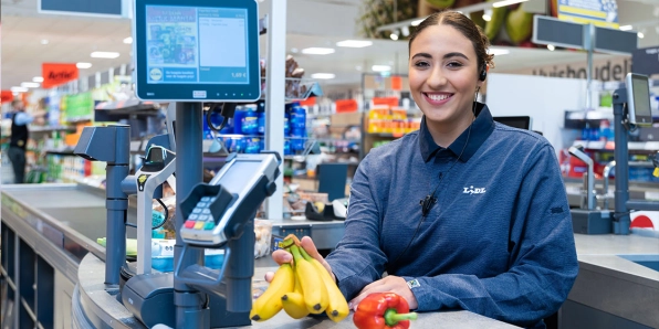 Bijbaner hulpkracht zit achter de kassa met groente en fruit
